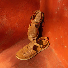 Load image into Gallery viewer, Pair of tan sandals on a red surface