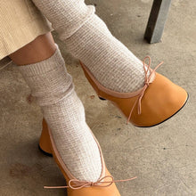 Load image into Gallery viewer, Person wearing tan shoes with bow details and white leg warmers on a concrete floor.
